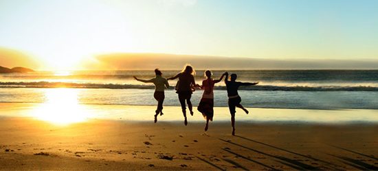 friends holding hands and jumping on beach