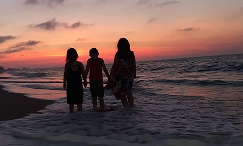 family holding hands in ocean at sunrise