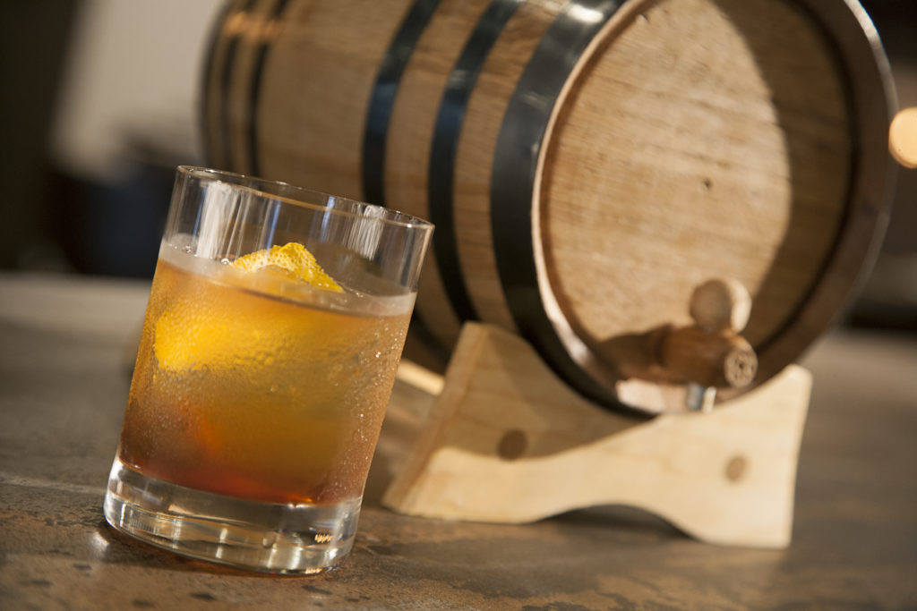 Strong waters old fashioned next to a barrel