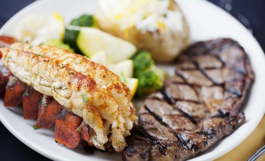 Steak on a plate with lobster, mashed potatoes, and vegetables for dinner