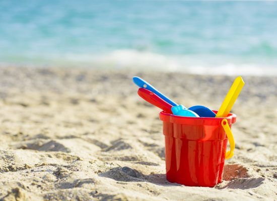 Red children's bucket with sand and toys on the seashore